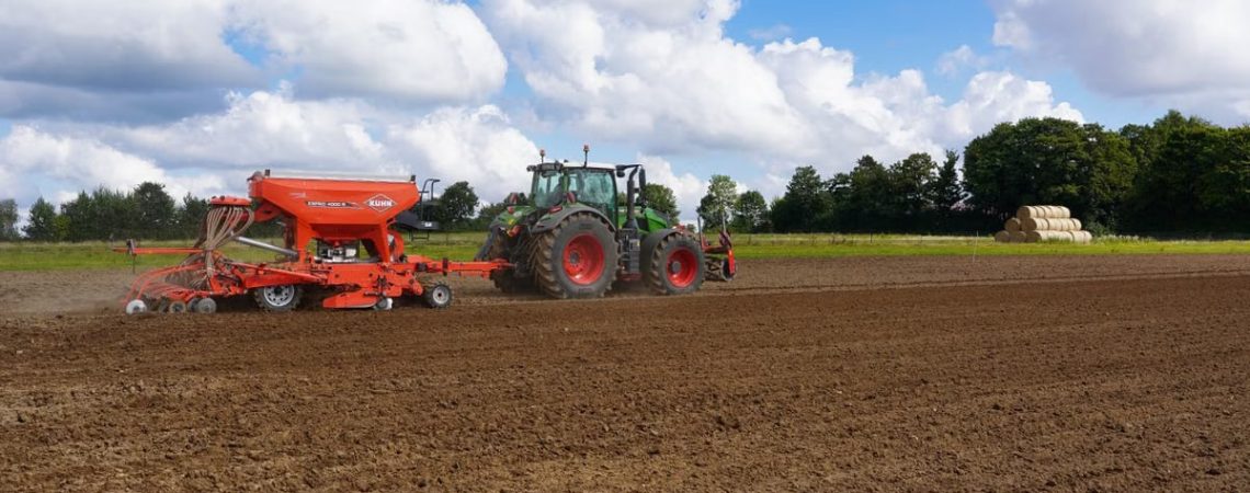 A modern tractor with a seeder working in a field in Schleswig-Holstein, Germany.