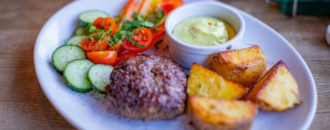 A well-presented gourmet meal featuring grilled patty, potatoes, and fresh vegetables.